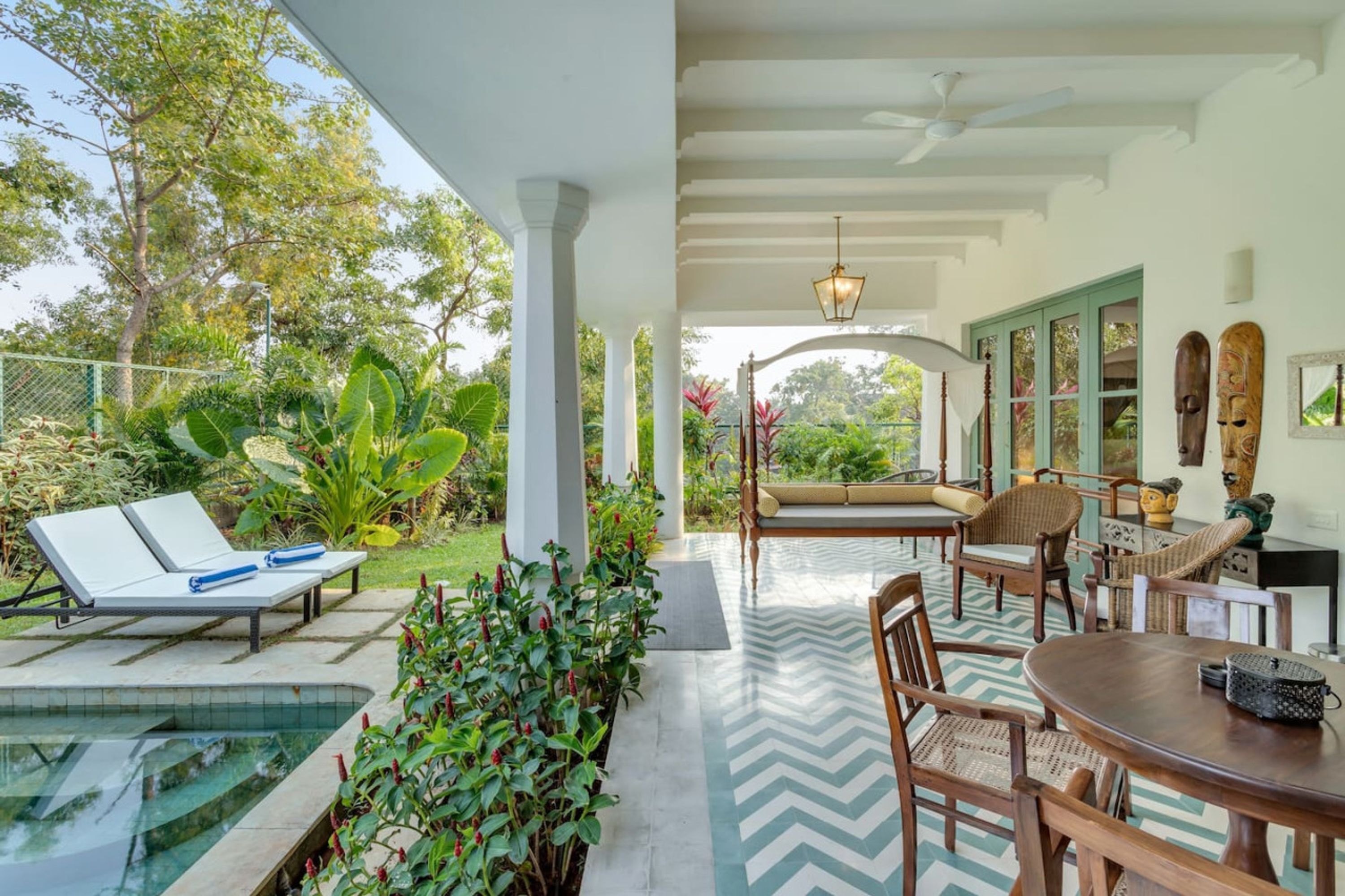 A covered outdoor area with a pool, lounge chairs, and a dining table.