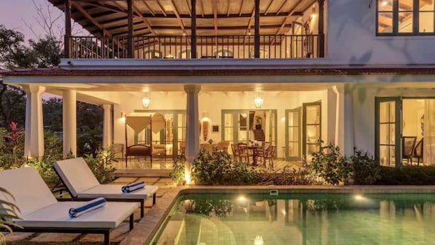 Una casa de dos pisos con piscina, mobiliario exterior y un patio cubierto.