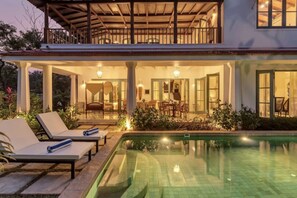 Une maison à deux étages dotée d’une piscine, d’un espace salon extérieur et d’un patio couvert.