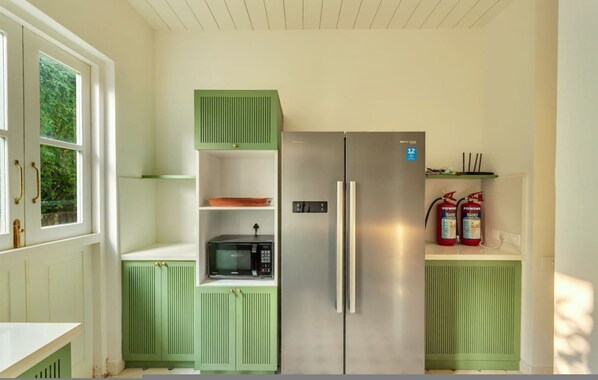 A compact kitchen with a built-in microwave, a stainless steel refrigerator, and a shelf with fire extinguishers.
