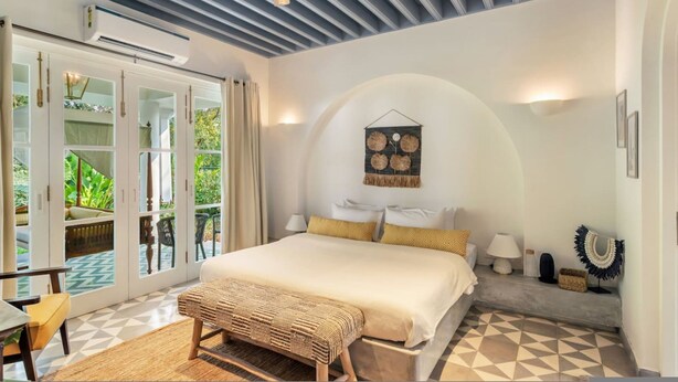A bedroom with a bed, a bench, a lamp, and a wall-mounted decoration. - Villa Eden - 10 Mins From Thalassa Vagator Beach (Vagator)