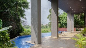 An outdoor pool area with a view of a lush garden and distant buildings. - 1BR Apt in Candolim With Pool 5 Mins From Beach (Candolim)