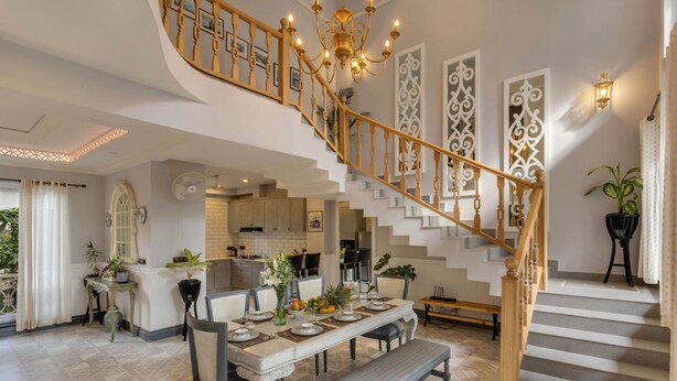A spacious living area with a grand staircase, a dining table set for four, and a kitchen in the background. - Villa Jaanzu - 4bhk With Private Pool in Saligao (Calangute)