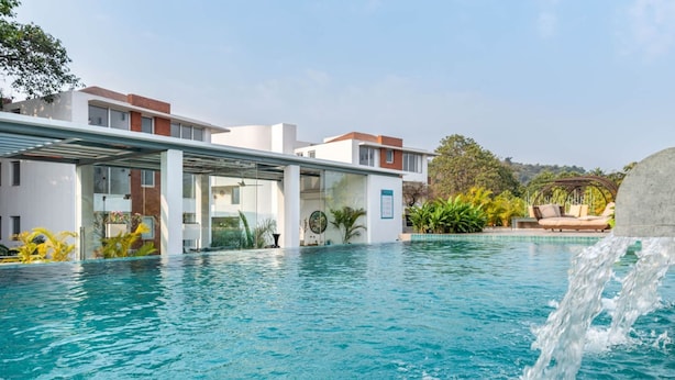 A modern hotel with a swimming pool, outdoor seating, and a waterfall feature. - El Arbol by Hireavilla -2br Apartment in Nerul (Nerul)
