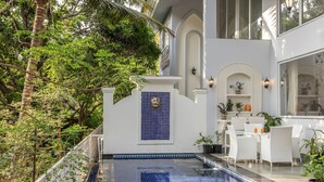 A pool area with a tiled floor, white outdoor furniture, and a decorative wall with a blue-tiled window. - The Hornbill Villa - 3bhk With Pvt Pool in Saligao (Calangute)