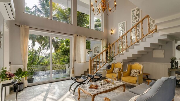 A spacious living area with a large window, a staircase, and a seating arrangement. - The Hornbill Villa - 3bhk With Pvt Pool in Saligao (Calangute)