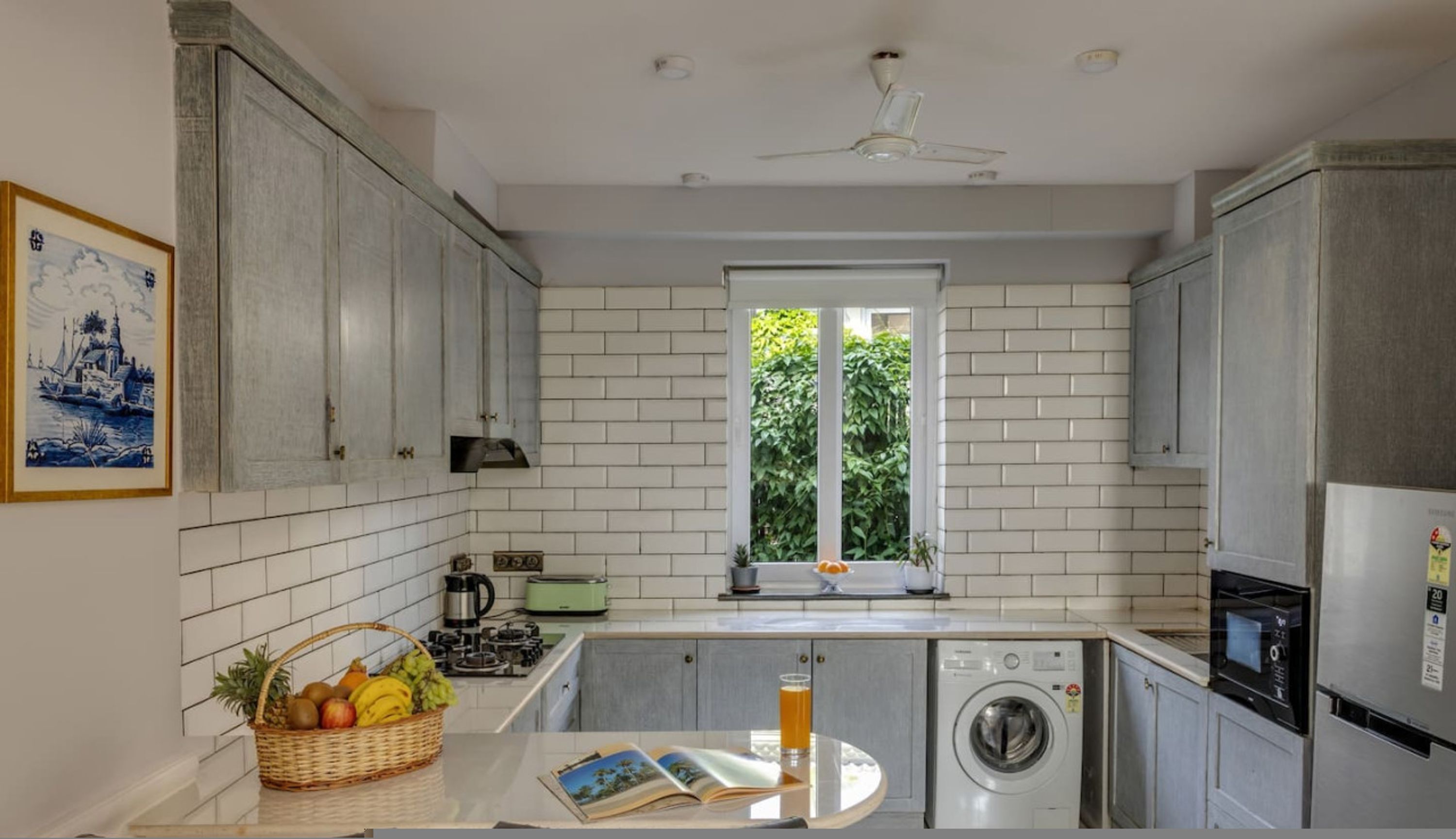 Een moderne keuken met witte tegels, een wasmachine en een raam met beplanting erbuiten.