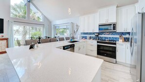 A modern kitchen with white cabinetry, a large island, and a view of palm trees outside. - Dolphin Days Lagoon Escape (Panama City)