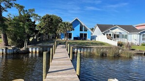 A wooden dock leading to a house with a blue exterior, surrounded by water and trees. - Dolphin Days Lagoon Escape (Panama City)