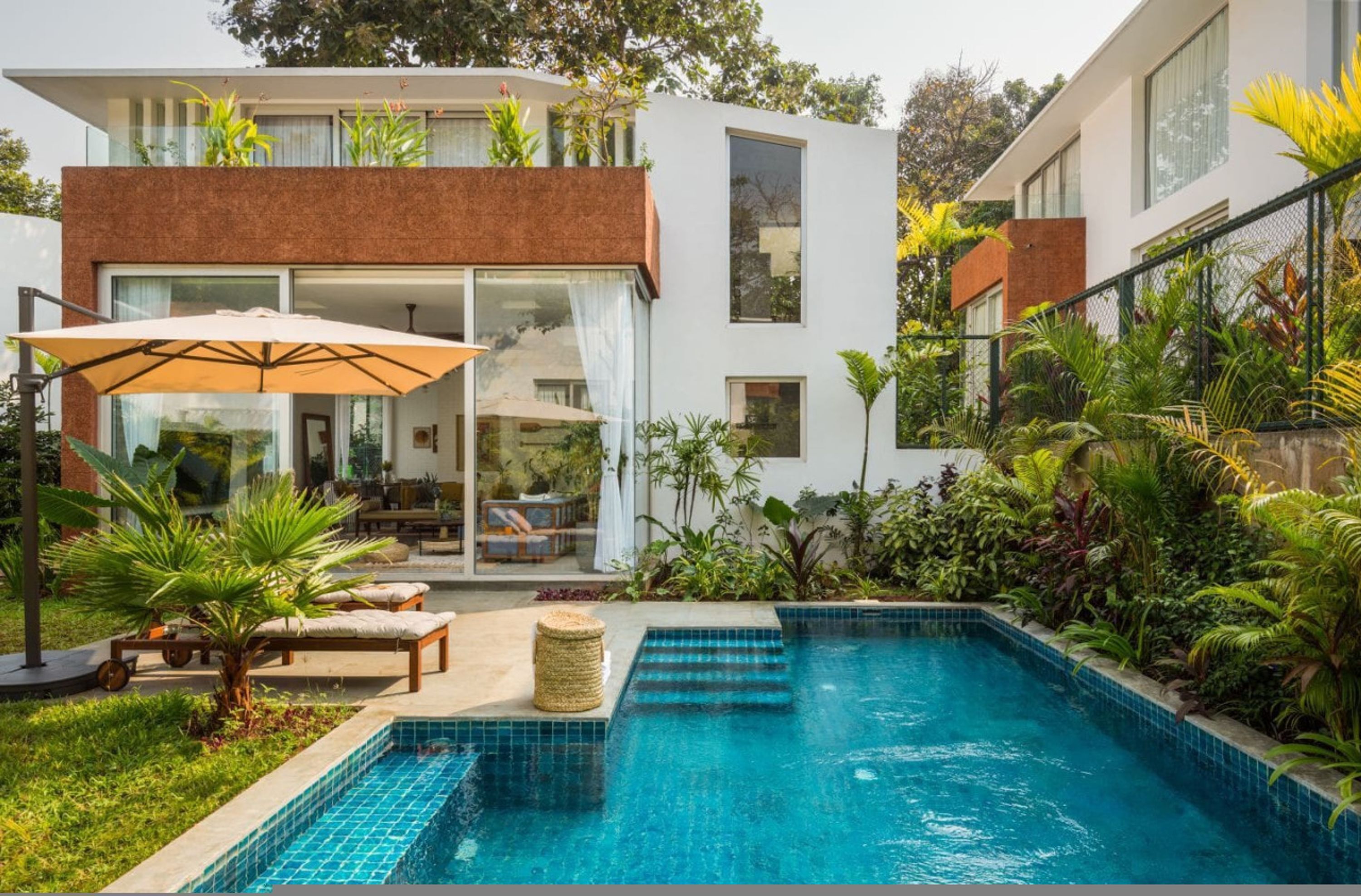 Una casa moderna con piscina, mobiliario exterior y exuberante vegetación.