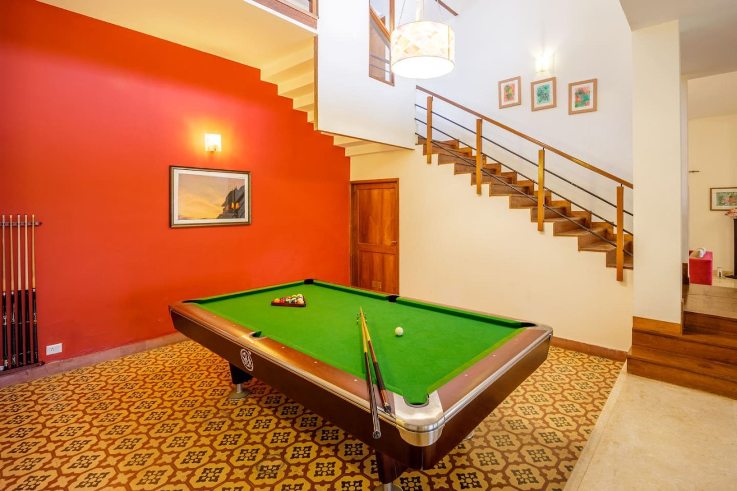 Ein Billardtisch in einem Raum mit roter Wand, einer Treppe und einem gerahmten Bild.