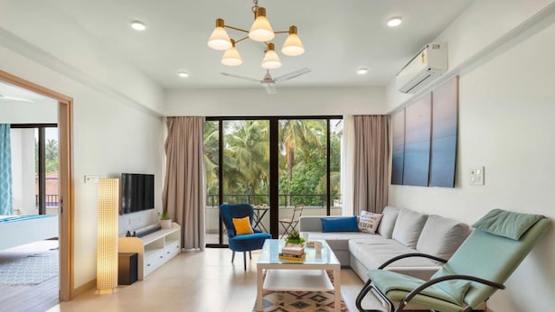 A modern living room with a sofa, a rocking chair, a coffee table, and a TV. - Spacious 3BR Apartment With Pool in Candolim (Candolim)