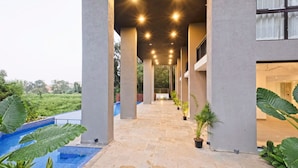 A covered walkway with columns, a pool, and potted plants. - Spacious 3BR Apartment With Pool in Candolim (Candolim)