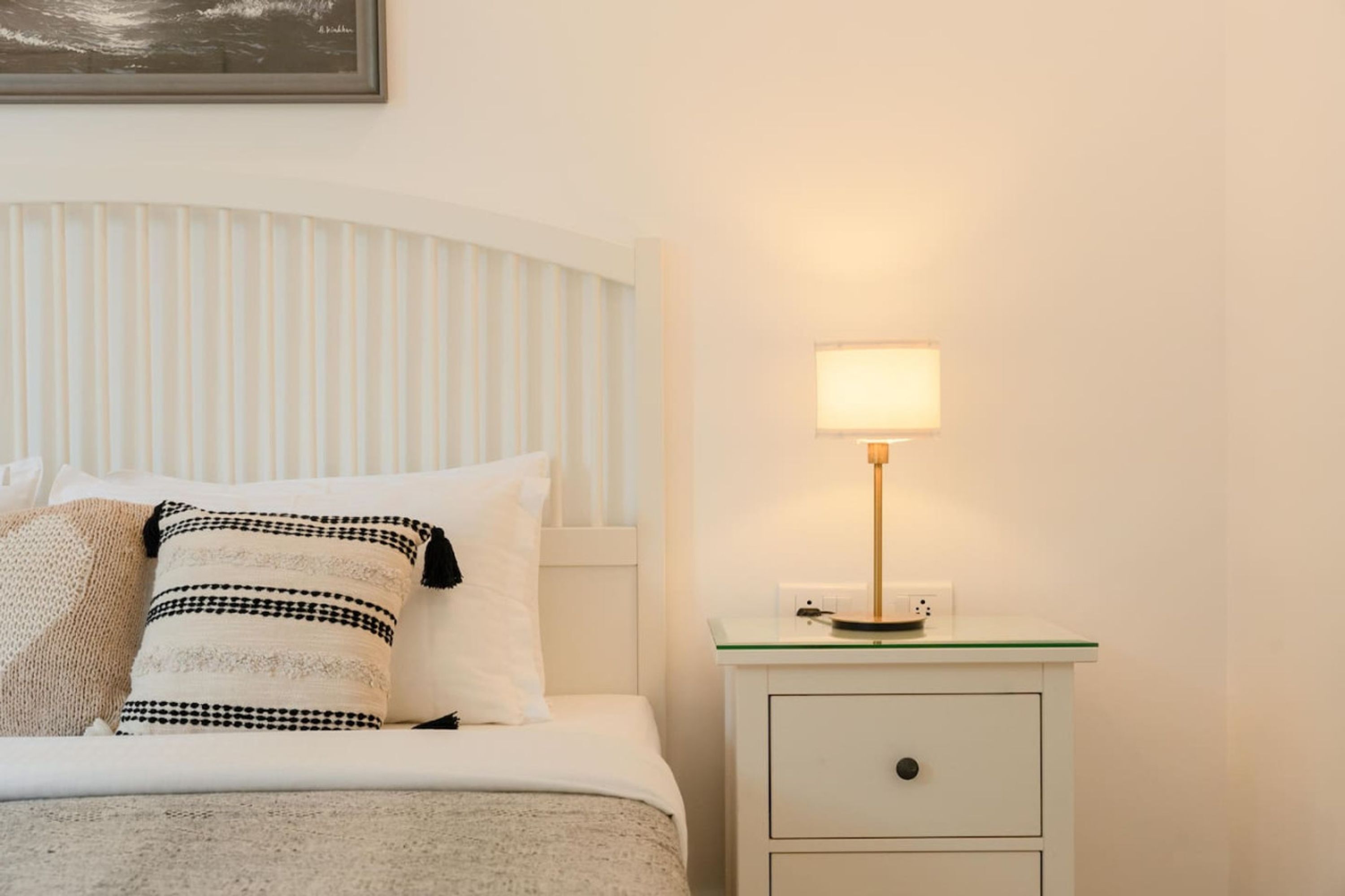 A neatly made bed with striped pillows, a bedside table with a lamp, and a framed picture on the wall.