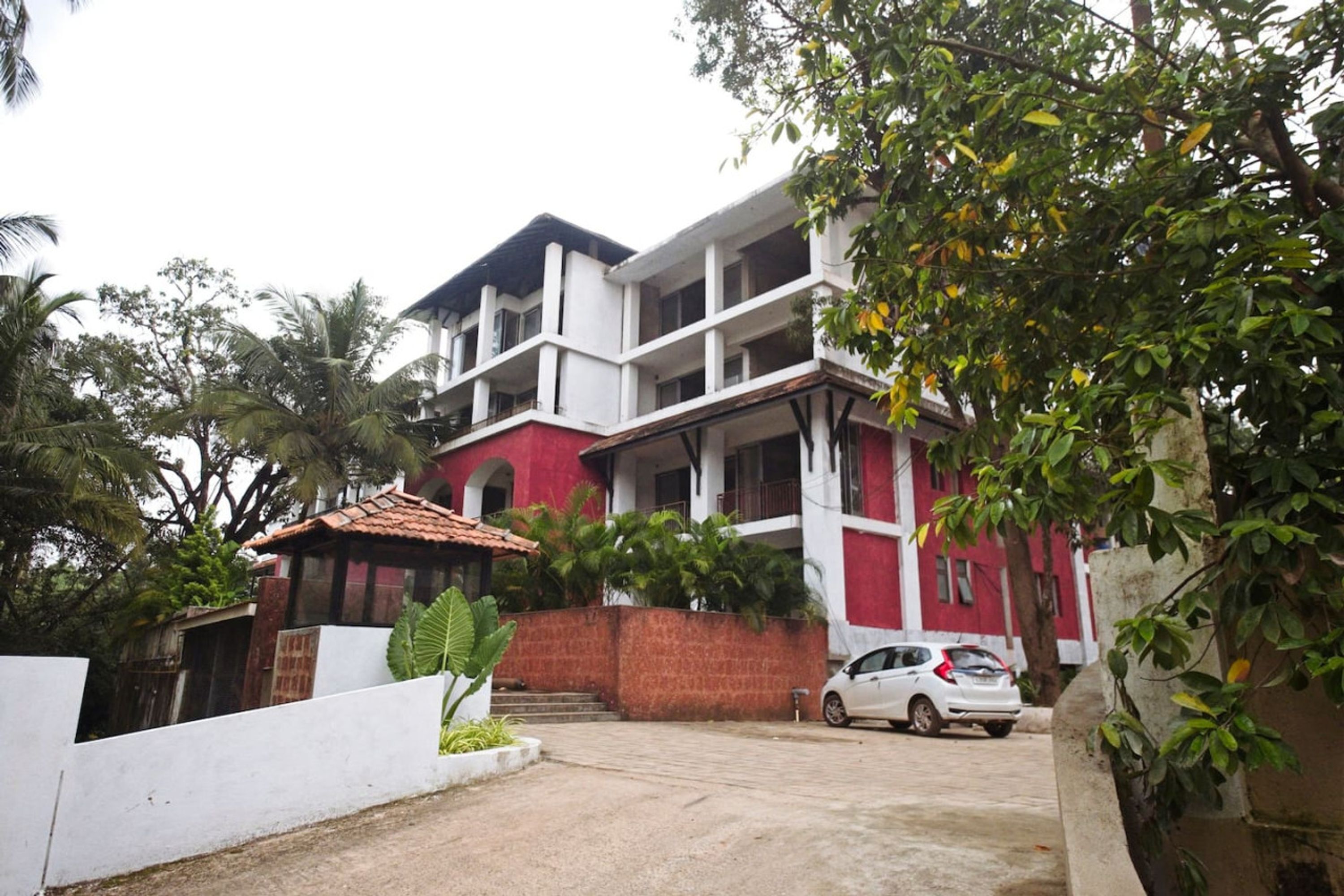 A two-story building with a red and white facade, a car parked in front, and a white wall with a small garden.