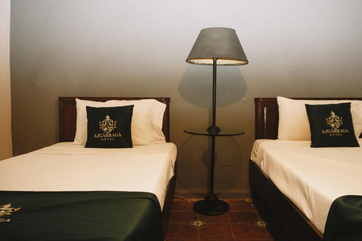 Two beds with matching pillows, a floor lamp, and a tiled floor.