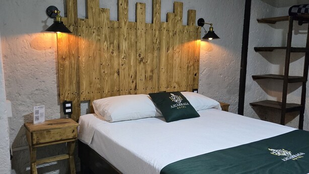 Un letto con testiera in legno, due lampade da comodino, un tavolino e una coperta verde.