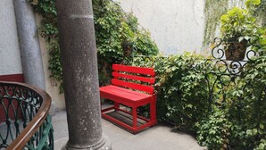 Una panchina rossa in un cortile con una colonna e vegetazione.