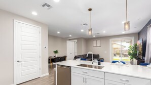Una cocina moderna con lavavajillas, armarios blancos e iluminación colgante.