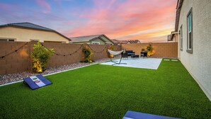 Un patio trasero con césped artificial, una hamaca y una zona de barbacoa.
