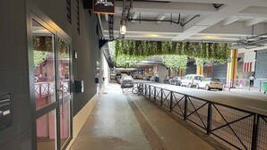 A covered walkway with a metal railing, a bike rack, and a view of parked cars and buildings in the background. - Fashion Lodge (Paris)