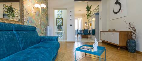 Una sala de estar moderna con un sofá azul, una mesa de centro y un comedor al fondo.