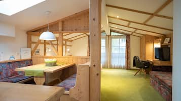 A cozy cabin interior with a wooden dining table, benches, a sofa, and a television.