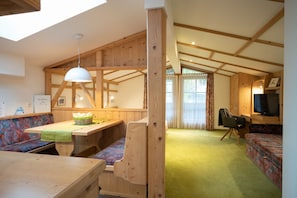 A cozy cabin interior with a wooden dining table, benches, a sofa, and a television. - Haus Katharina - Dorfblick (Kaprun)