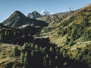 A mountainous landscape with a winding road, a ski lift, and a building with a view of the mountains. - Haus Katharina - Dorfblick (Kaprun)