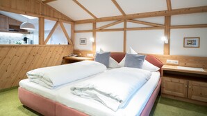 Een slaapkamer met een groot bed, houten balken, een raam, een nachtkastje en een bijzettafeltje.
