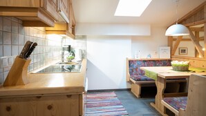 Een keuken met houten kastjes, een betegelde spatwand, een spoelbak en een eethoek met banken en een tafel.