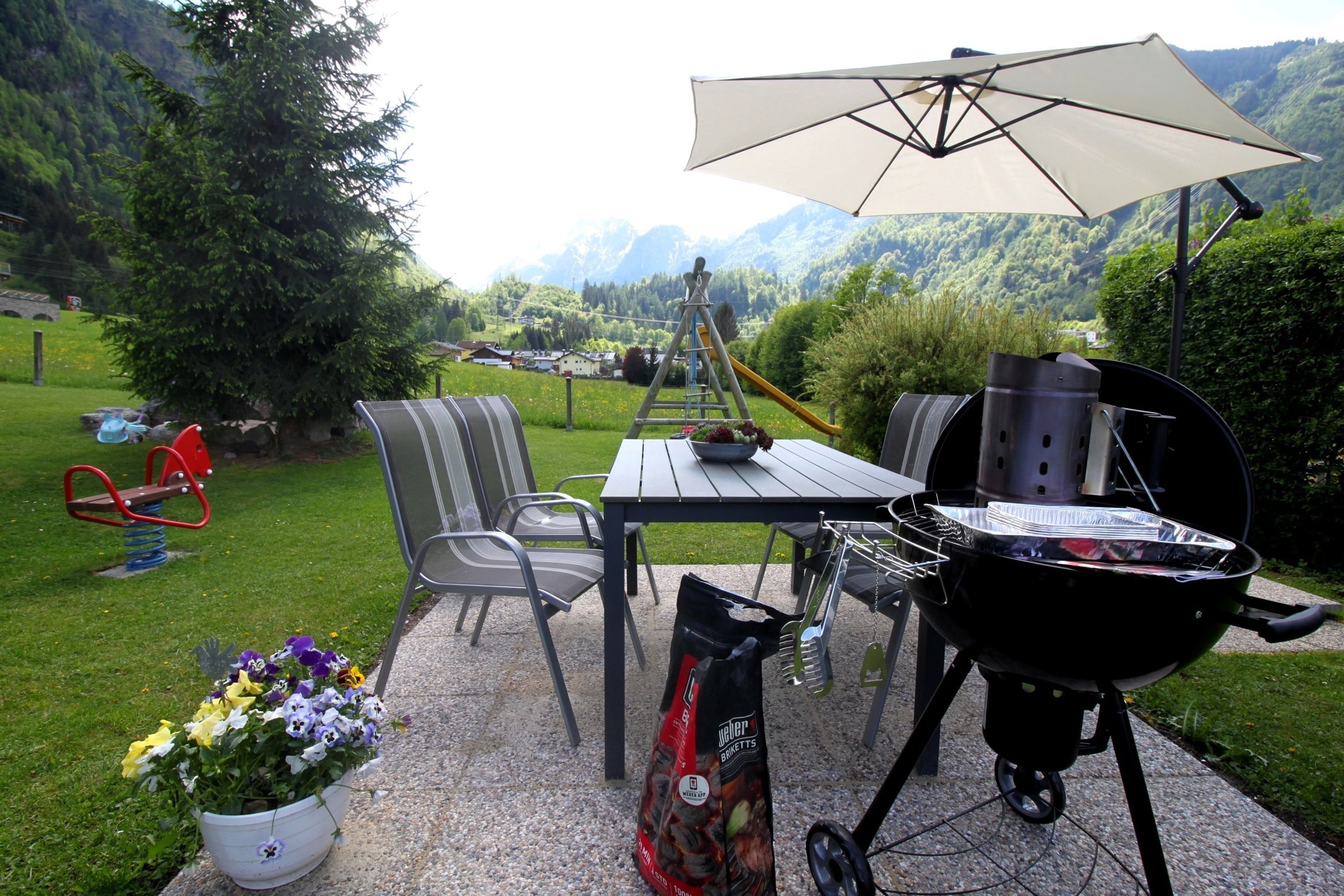 An outdoor patio with a grill, chairs, a table, and a potted plant.