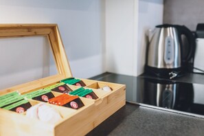 Eine Holzkiste mit Fächern, gefüllt mit verschiedenen Gegenständen, steht auf einer Arbeitsplatte neben einem Wasserkocher.