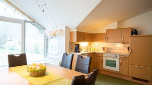 A modern kitchen with wooden cabinets, a dining table with chairs, and a basket of bread. - Haus Katharina - Kitzsteinhornblick (Kaprun)