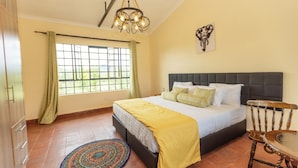 A bedroom with a bed, a wooden chair, a round rug, a window with curtains, and a chandelier. - Ene Hacienda (Maili Tisa)