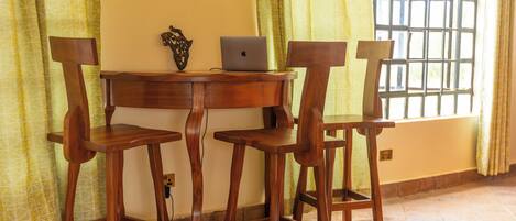 Un comedor con una mesa de madera y cuatro sillas, una computadora portátil sobre la mesa, y una ventana con celosía de metal.