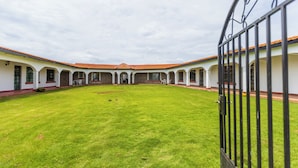 A courtyard with a green lawn and a building with a tiled roof and arched windows. - Ene Hacienda (Maili Tisa)