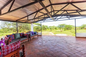 A covered outdoor seating area with a bench and cushions, a tiled floor, and a view of the surrounding landscape. - Ene Hacienda (Maili Tisa)