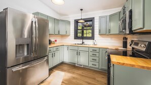 Una cocina moderna con electrodomésticos de acero inoxidable, armarios verde claro y encimera de madera.