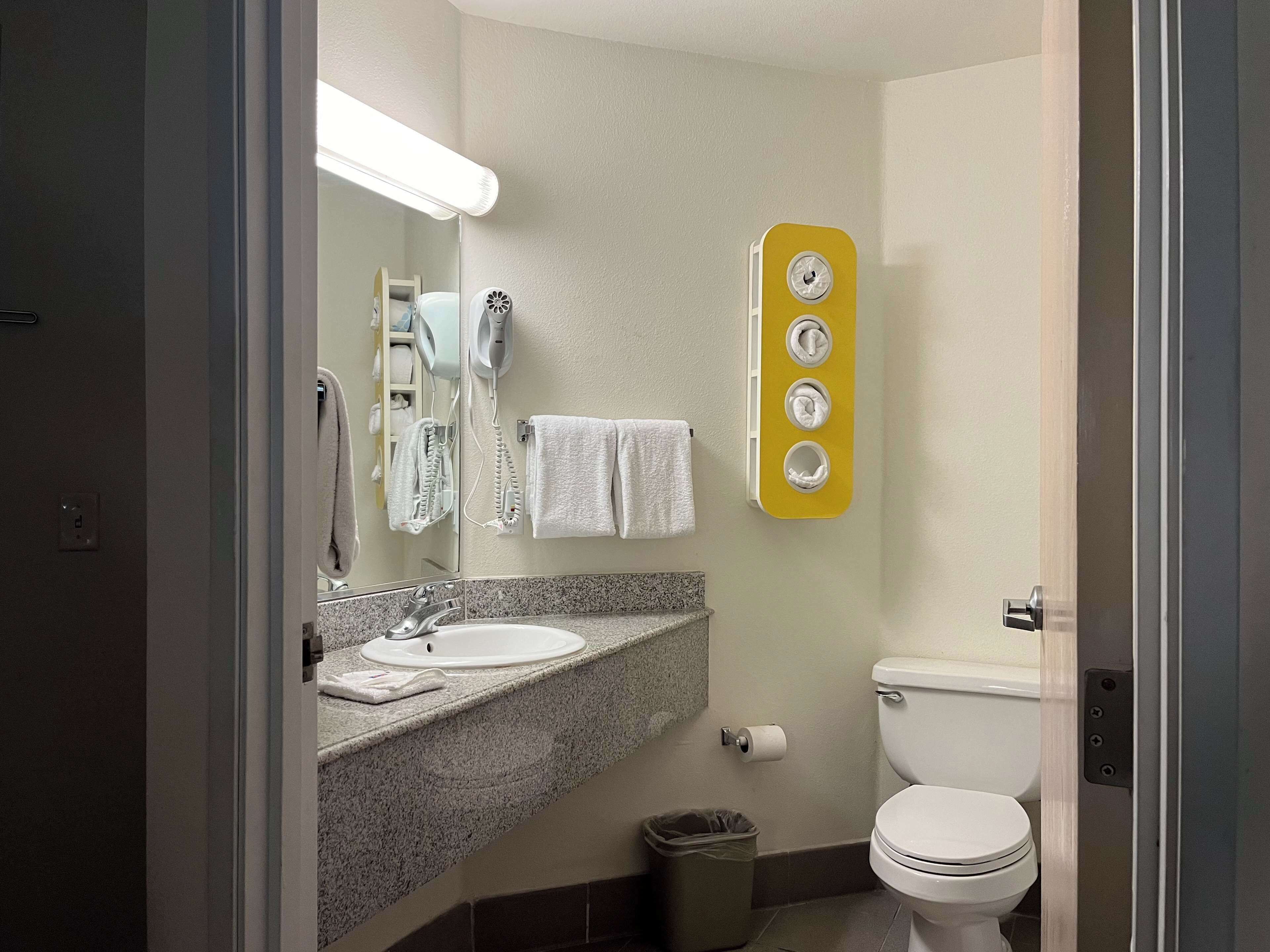 Un baño con lavamanos, espejo, toallero y retrete.