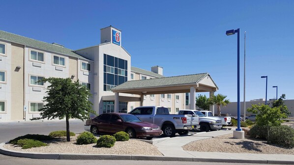 A motel with a covered parking area, multiple vehicles parked, and a clear sky. - Studio 6 – Las Cruces, NM - Telshor (Las Cruces)