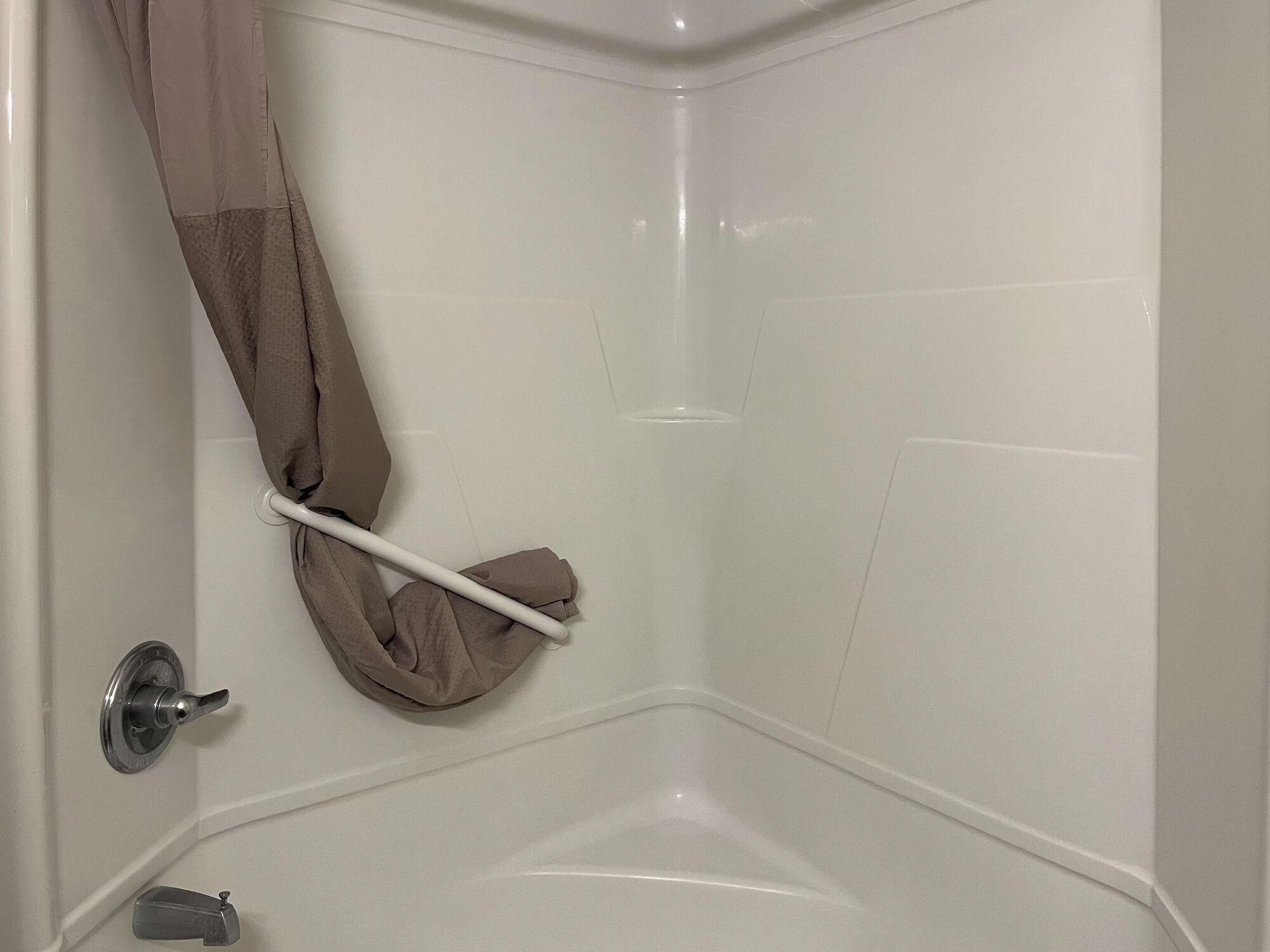 A corner of a bathroom with a white bathtub, a towel rack with a towel, and a shower control knob.