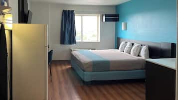 A bedroom with a bed, a desk, a chair, a window with curtains, and a wall-mounted air conditioner.