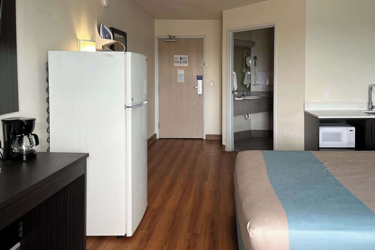 A hotel room with a bed, a refrigerator, a coffee maker, a microwave, and a bathroom with a sink and mirror.
