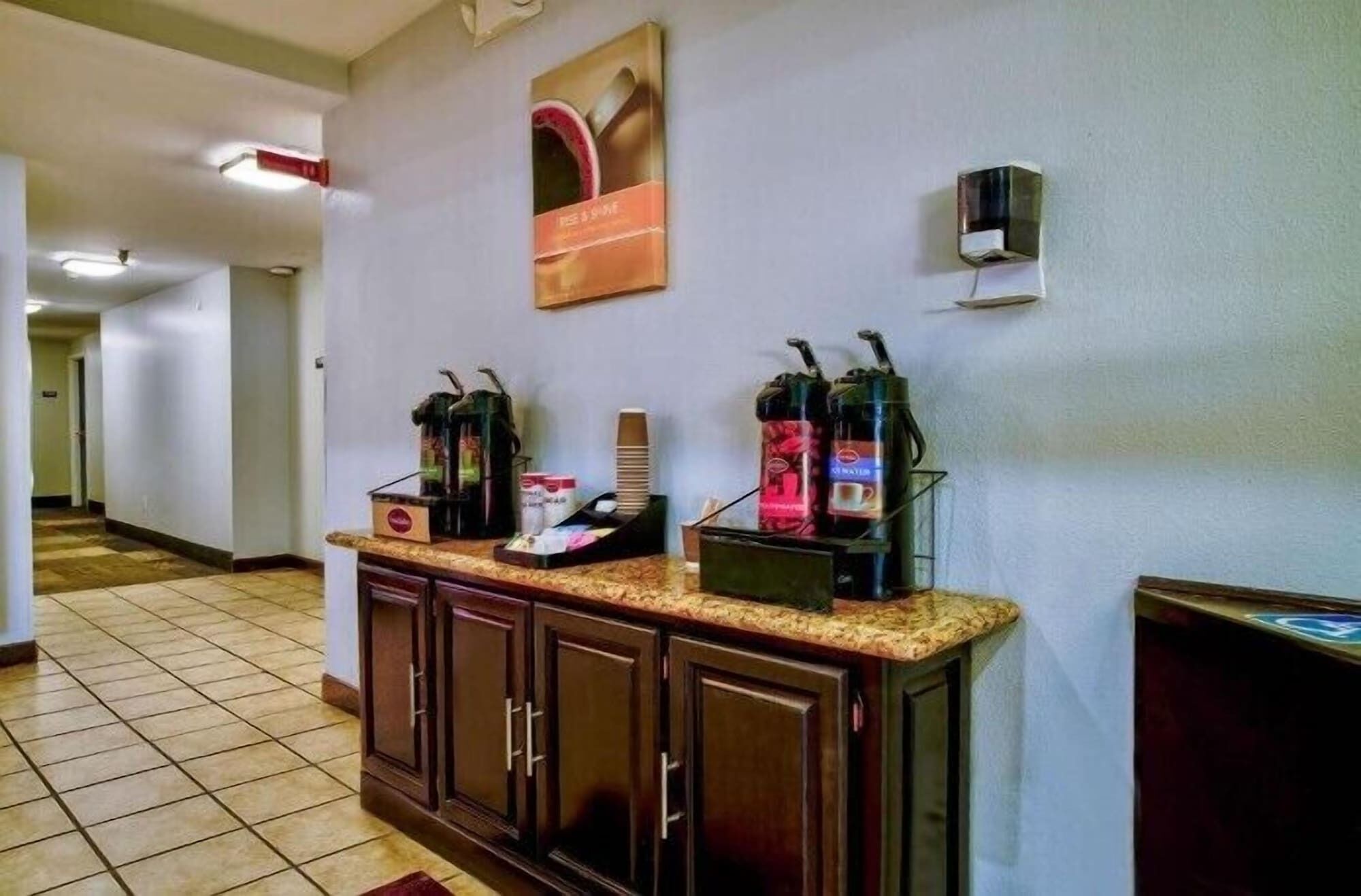Zona de recepción de hotel con estación de café, un cuadro en la pared y un pequeño altavoz.