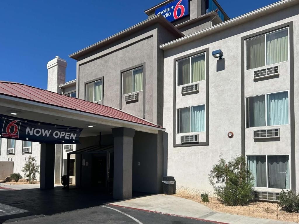 Un motel con un letrero que dice 'NOW OPEN', una zona de estacionamiento techada y un cielo despejado.