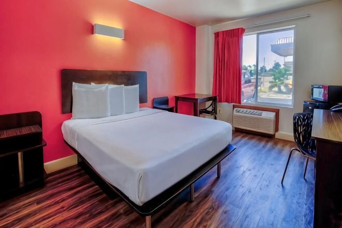 Habitación de hotel con cama, escritorio, silla, mesita y ventana con cortinas.