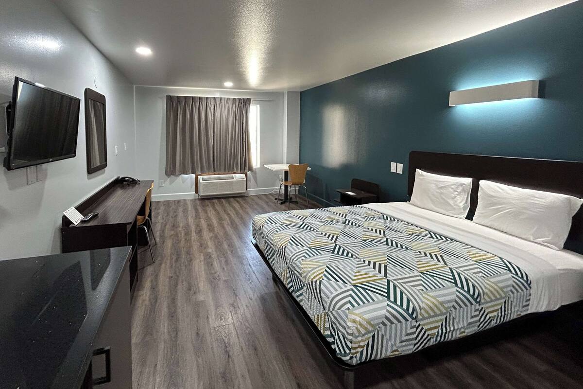 A modern hotel room with a large bed, a desk, a chair, a TV, and a window with curtains.