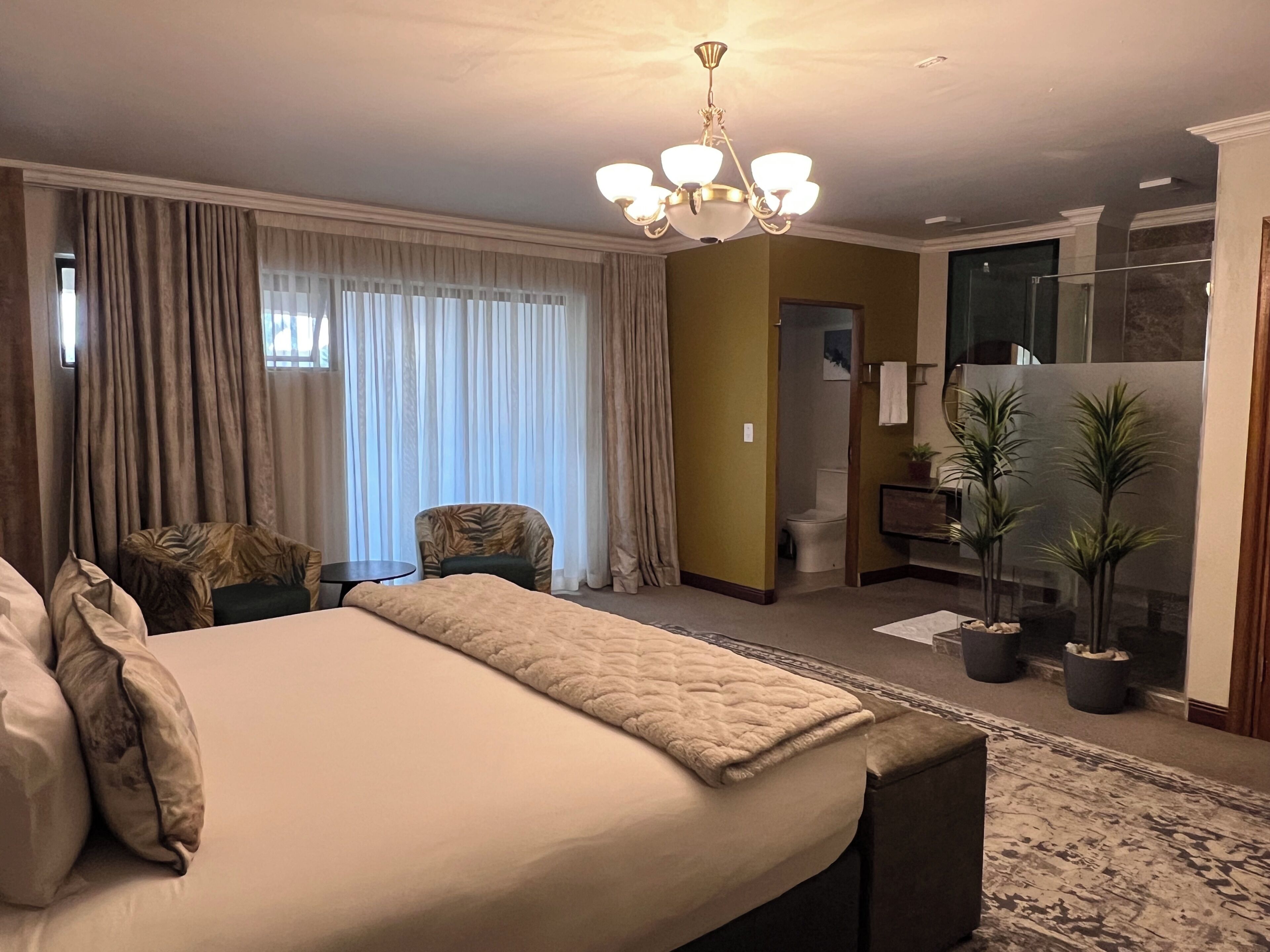Habitación de hotel con una cama grande, una silla, una mesita, un baño y un balcón con plantas.