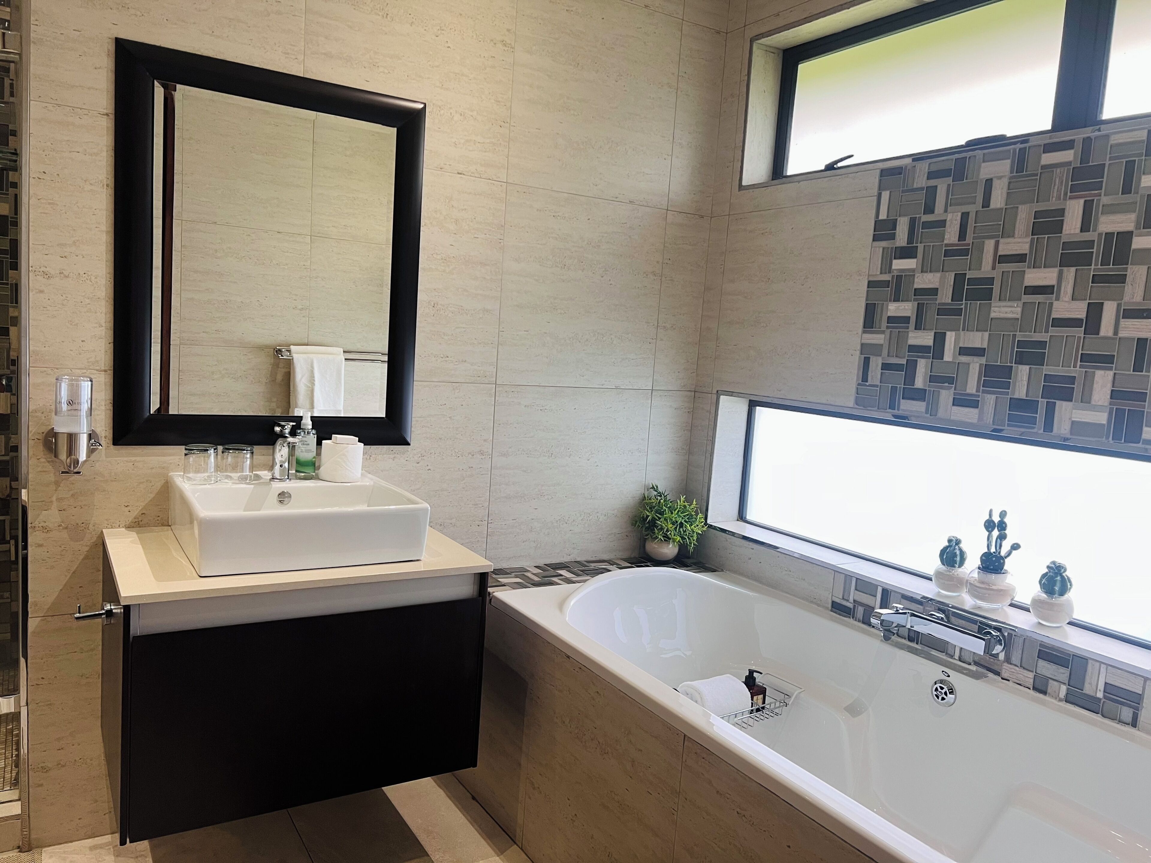 Un baño moderno con una bañera grande, un lavamanos con espejo y una ventana con vistas.